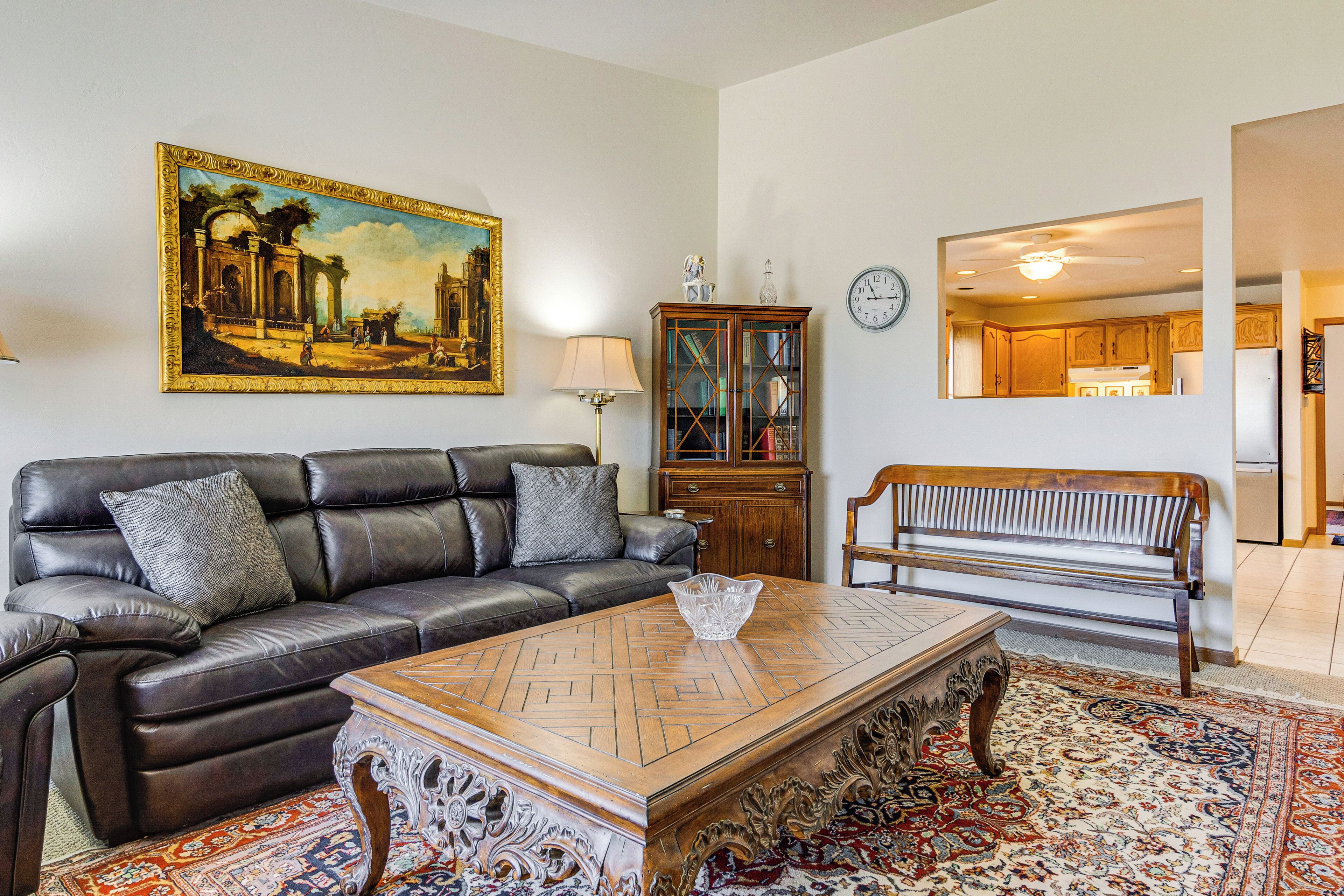 A living room with a leather sofa, a wooden coffee table, a bench, a cabinet, and a large painting on the wall.