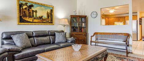 A living room with a leather sofa, a wooden coffee table, a bench, a cabinet, and a large painting on the wall.