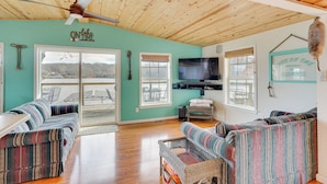 A cozy living room with a wooden ceiling, a large TV, and a view of a lake. - Fish & Boat on Lake of the Ozarks: Waterfront Home (Edwards)