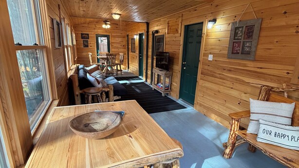 A wooden cabin interior with a dining table, wooden chairs, a sofa, and a fireplace.