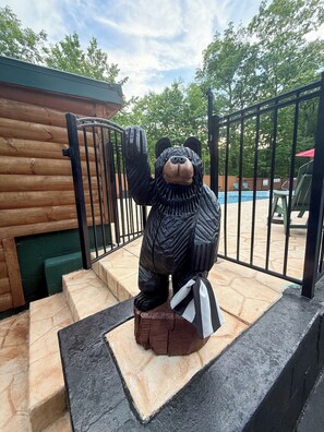 Eine Bärenstatue auf einer Plattform mit Treppen, einem Pool und einem Holzzaun im Hintergrund.