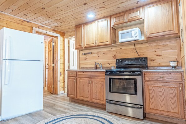 A kitchen with wooden cabinets, a stainless steel refrigerator, a microwave, and a stove.