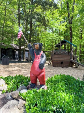 A bear statue holding an American flag, surrounded by greenery and a wooden structure.