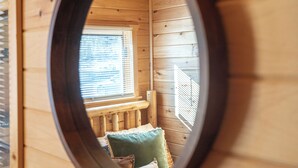 A circular window view of a wooden cabin room with a bed, pillows, and a window with blinds.