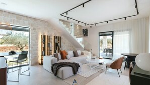 Un salon moderne avec un canapé blanc, une table basse et une bibliothèque. Un escalier mène à un niveau supérieur.