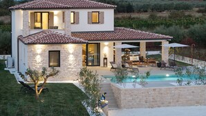 Une maison à deux étages avec une piscine, des murs en pierre et un espace salon extérieur.