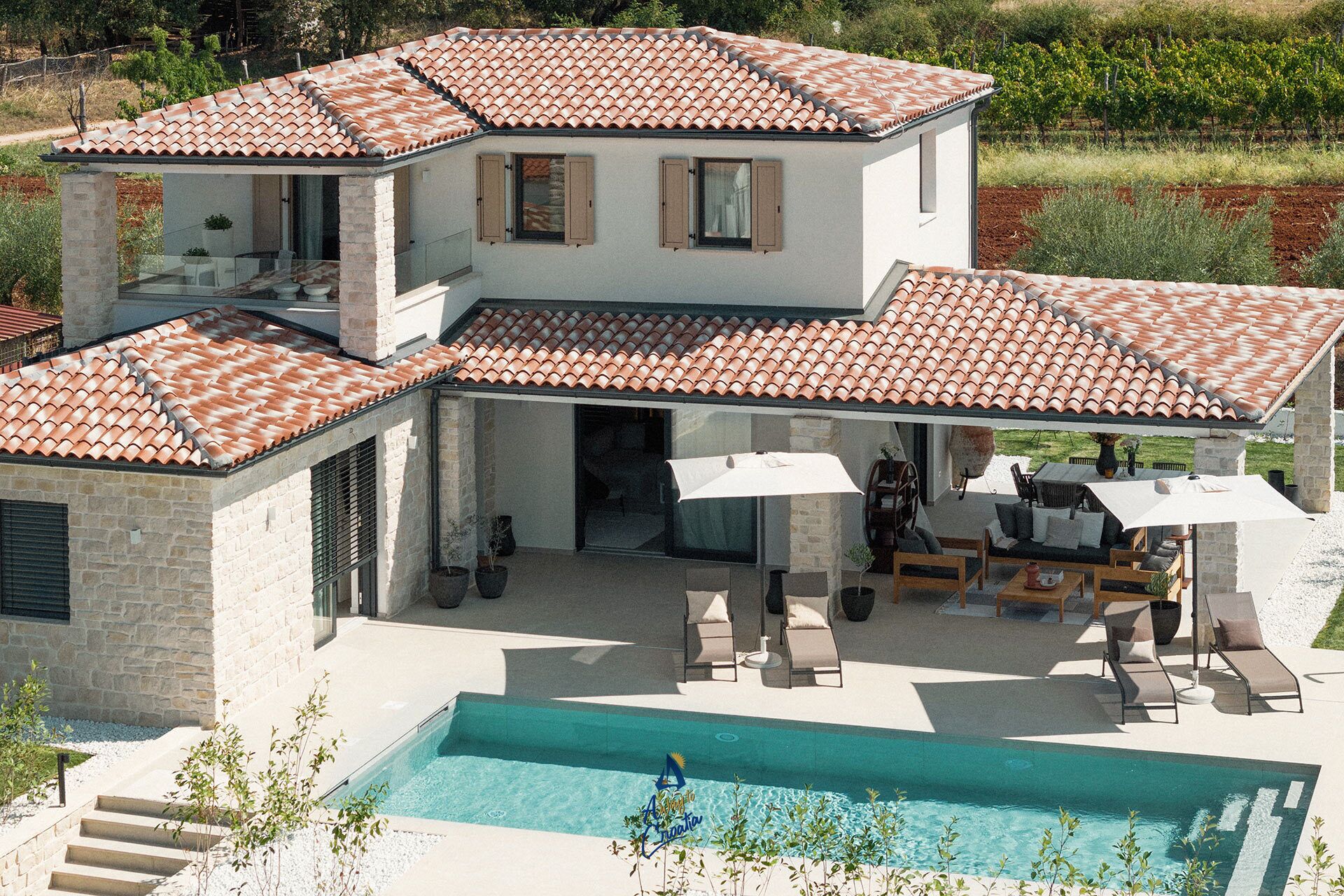 A two-story house with a swimming pool, outdoor seating area, and a vineyard in the background.
