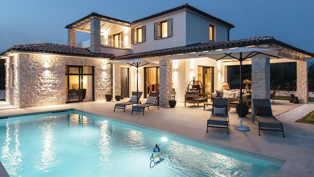 Une maison à deux étages avec une piscine, un espace salon extérieur et des murs en pierre.