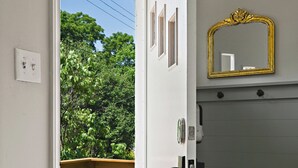 A room with a door leading to a balcony, a mirror on the wall, and a welcome mat at the entrance.