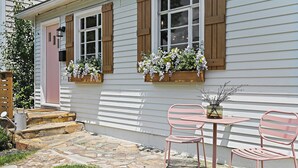 A house with a stone staircase leading to a door, a small patio with a table and two chairs, and flower boxes on the windowsills.