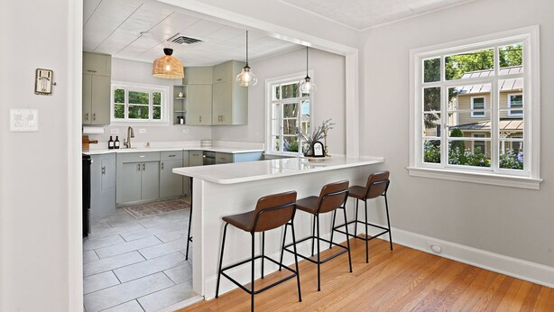 A modern kitchen with a large island, bar stools, pendant lighting, and a view of the outside through a window.