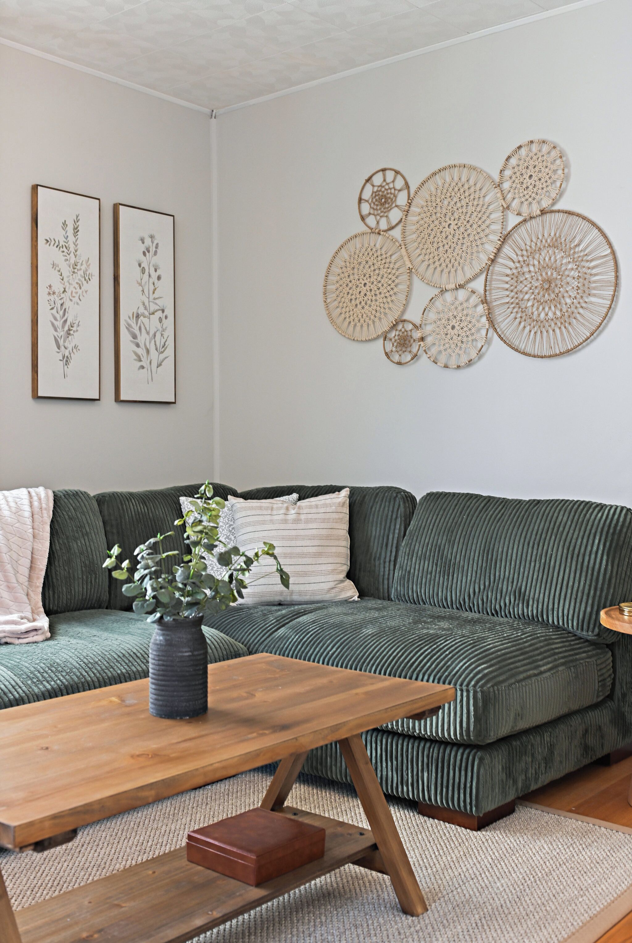 A living room with a green sofa, a wooden coffee table, and wall art.
