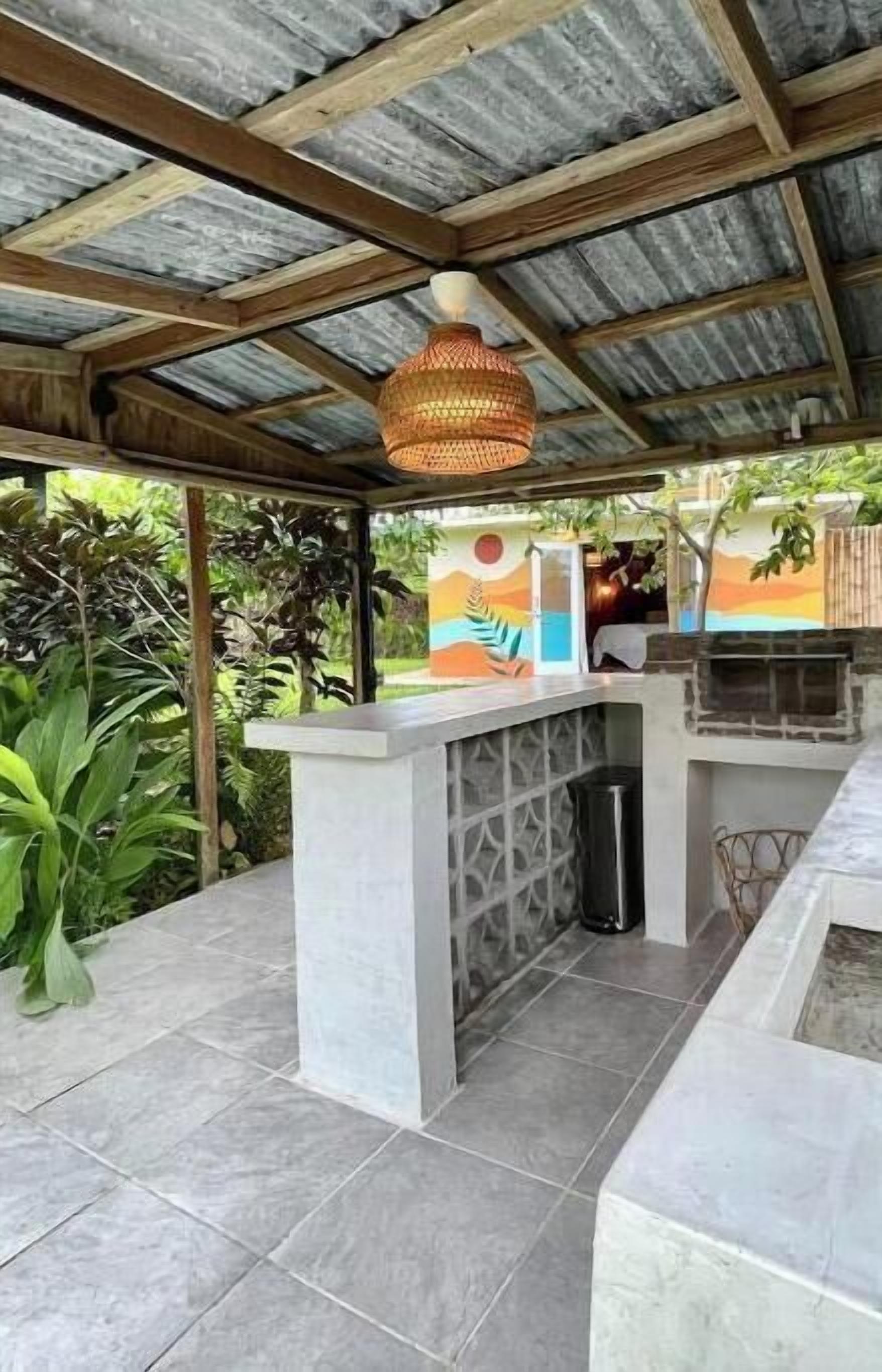 An outdoor kitchen area with a concrete countertop, a hanging light fixture, and a tiled floor.