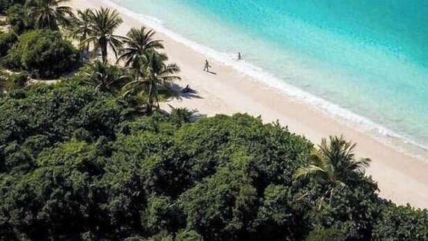 A beach with clear turquoise waters, surrounded by dense green vegetation and hills in the background. - The Sunset Shack (Ceiba)
