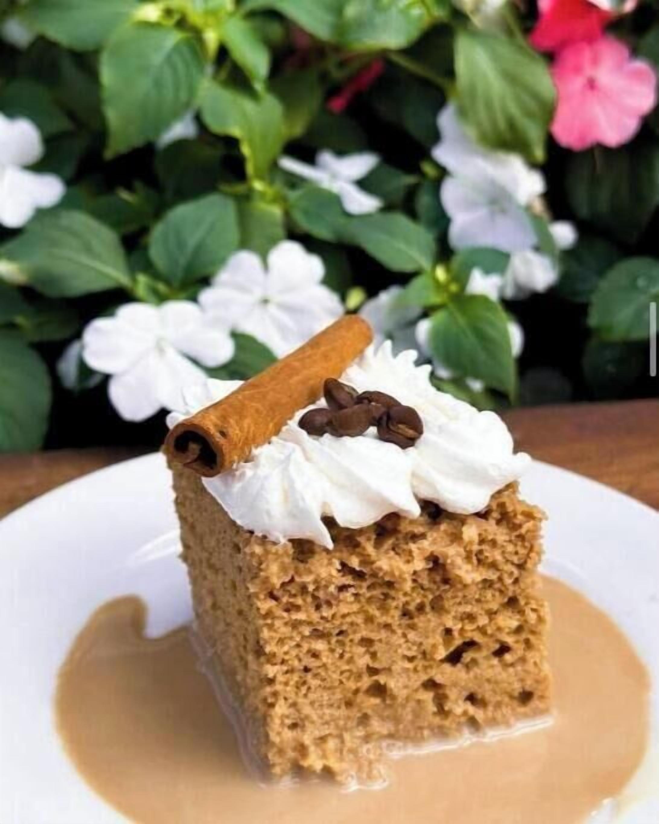 Ein Stück Kuchen mit Schlagsahne und einem Zimtstange, serviert auf einem weißen Teller mit Karamellsauce.