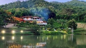 A two-story building with a balcony, surrounded by lush greenery and a calm lake. - The Sunset Shack (Ceiba)