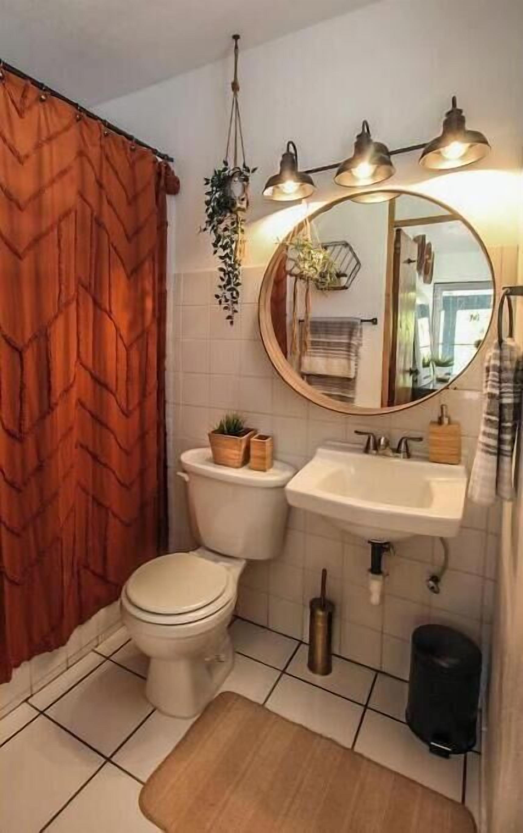 Une salle de bain avec des toilettes, un lavabo et un miroir. On y trouve également des plantes et un rideau de douche.