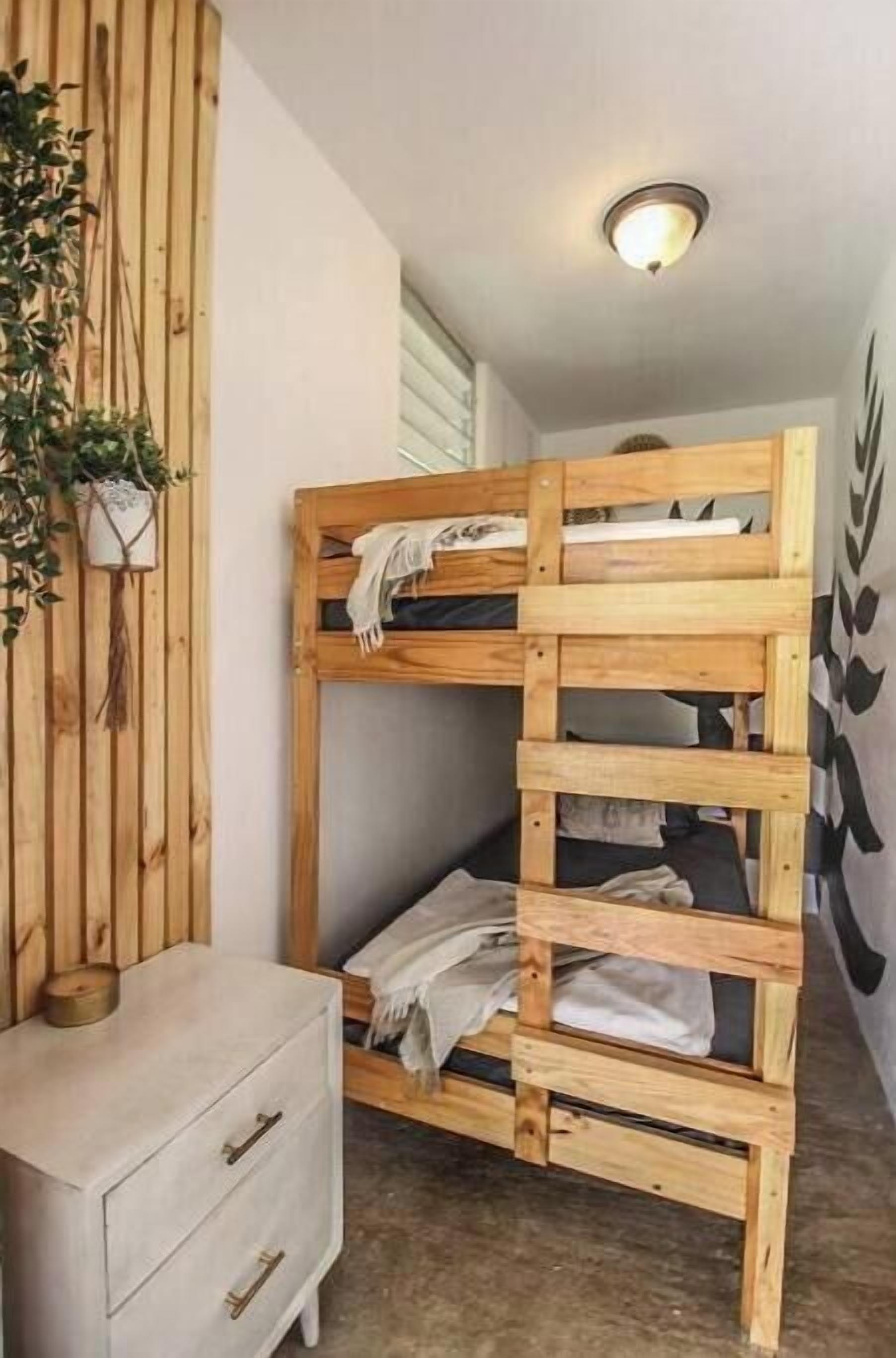 Un lit superposé avec une structure en bois, une petite table de chevet et une plante fixée au mur.