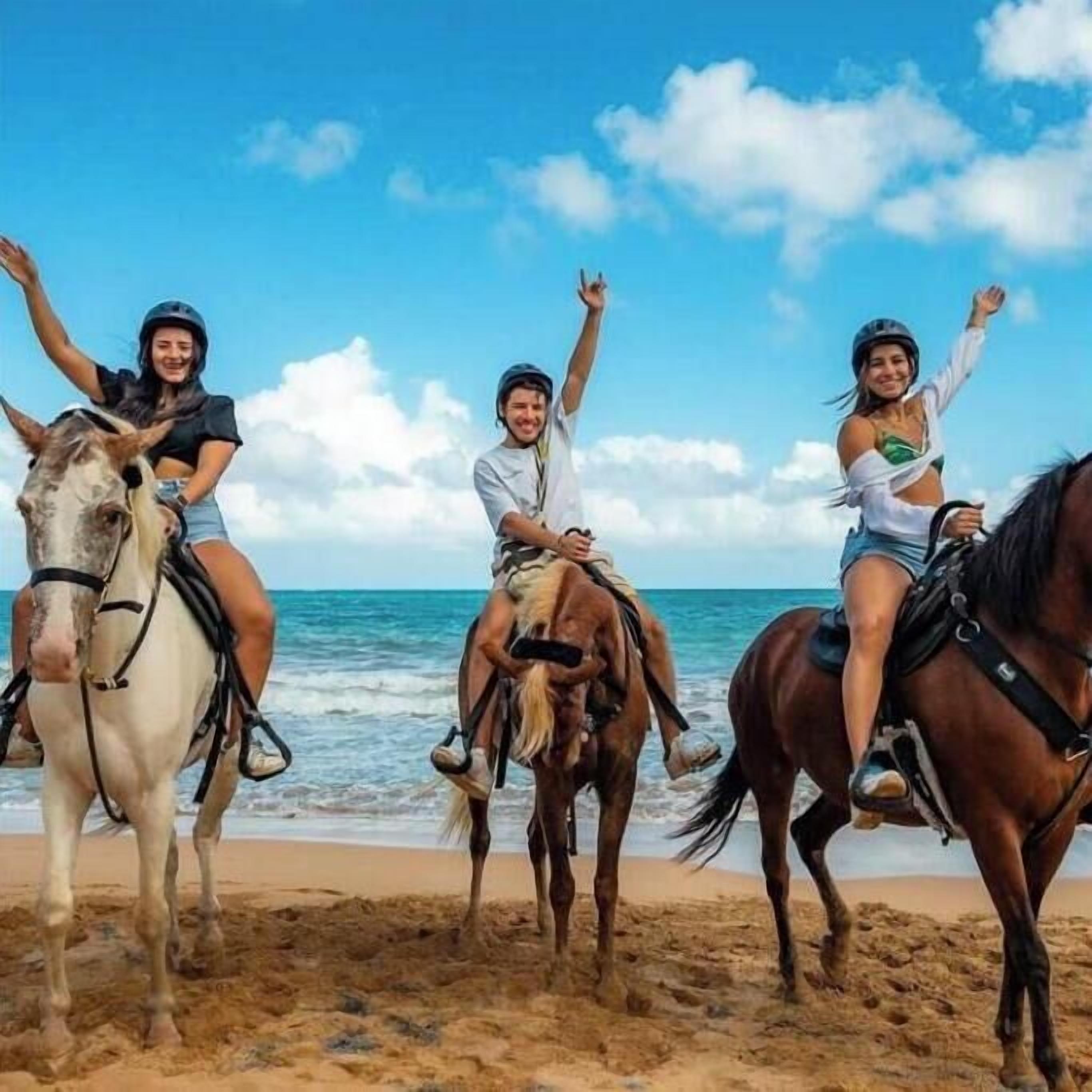 Tre persone cavalcano cavalli su una spiaggia, con l'oceano sullo sfondo.