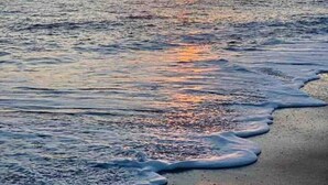 Un coucher de soleil sur une mer calme, avec des éoliennes visibles au loin.