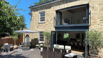 Un bâtiment en pierre de deux étages doté d’un patio aménagé avec du mobilier d’extérieur et un grand parasol.