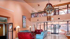Eine geräumige Lobby mit einer roten und blauen Sofagarnitur, einem großen Kronleuchter und Blick ins Freie durch große Fenster.