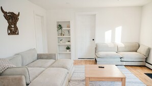 Een moderne woonkamer met een beige bank, een houten salontafel en een witte deur.