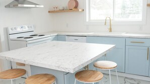 Een moderne keuken met een marmeren aanrechtblad, witte kasten en een groot kookeiland met barkrukken.