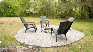 Een ronde zithoek met vier Adirondack-stoelen en een vuurkorf in het midden, omgeven door een grindrand.