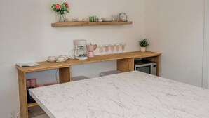 Een kleine keuken met een marmeren aanrecht, houten krukken en een plank met keukengerei.