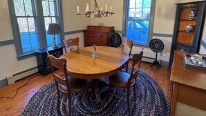 A dining room with a round wooden table, four chairs, a chandelier, and a cabinet with decorative items. - Charming Rockport, Maine 3BR – Walk to Picturesque Harbor & Downtown (Rockport)