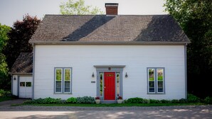 A white single-story house with a red front door, two windows on the ground floor, and a chimney. - Charming Rockport, Maine 3BR – Walk to Picturesque Harbor & Downtown (Rockport)