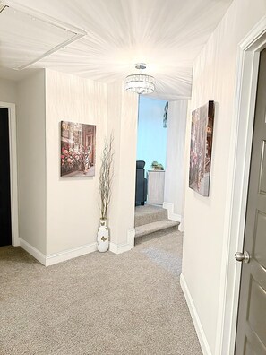 A hallway with a chandelier, framed artwork, and a vase with branches.