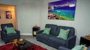 A living room with a dark blue sofa, a red rug, and a painting of a coastal scene. - Spacious 5-bedroom house with AC and WiFi in charming Lawrenceville (Lawrenceville)
