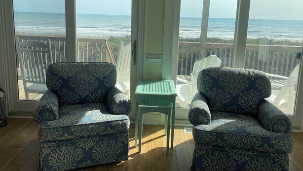 Une pièce avec deux fauteuils à motifs, placés face à une porte-fenêtre coulissante qui donne sur un balcon offrant une vue sur l’océan.