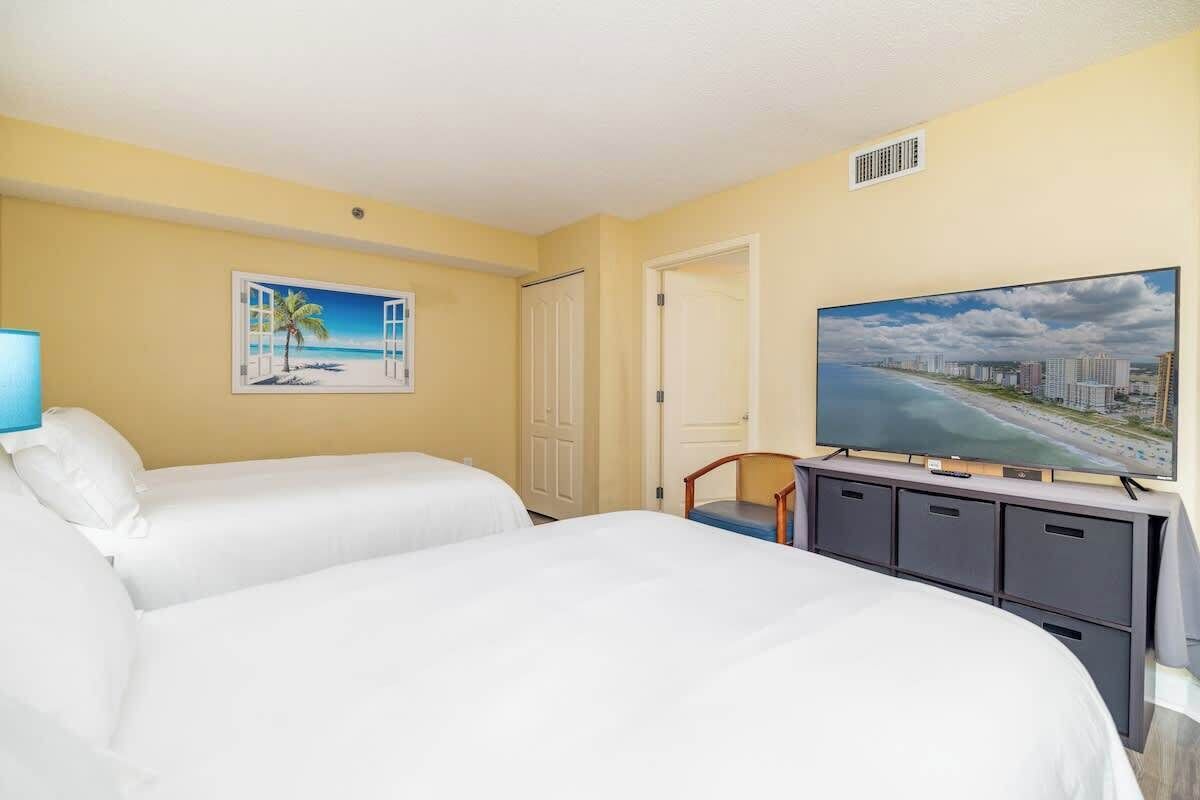 Habitación de hotel con dos camas, un televisor y un cuadro de una playa.
