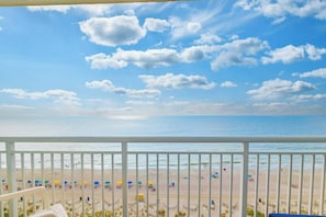 A beach view from a balcony with a railing, beach umbrellas, and people in the distance.