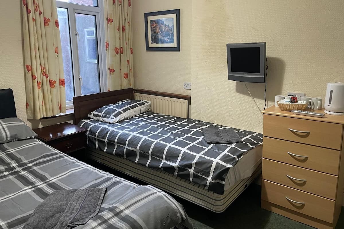 A bedroom with a bed, a bedside table, a dresser, a television, and a window with curtains.