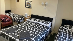 A hotel room with three beds, each with a black and white checkered bedspread. There is a chair with a floral cushion, a small table with a kettle and cups, and a framed picture on the wall. - Red Rose Hotel (Blackpool)