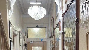 A hallway with a red carpet, a chandelier, framed pictures, and a door with a glass panel. - Red Rose Hotel (Blackpool)