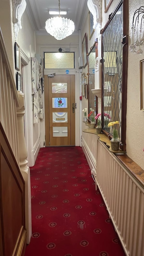 A hallway with a red carpet, a chandelier, framed pictures, and a door with a glass panel.