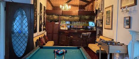 Una mesa de billar con dos tacos, una zona de bar con televisión y un área de estar con un sofá y sillones.