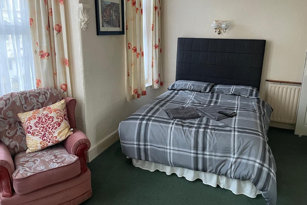 A bedroom with a bed, a chair, a framed picture on the wall, and a radiator.