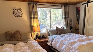 Une pièce chaleureuse avec deux lits en bois, une fenêtre avec des rideaux, une lampe fixée au mur et un ours en guise de décoration.