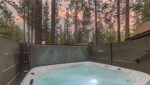 Un bain à remous installé à l’extérieur, entouré de grands arbres et délimité par une clôture en bois.