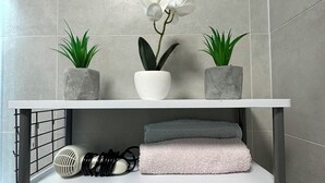 A bathroom vanity with a white shelf, two potted plants, a white orchid, a towel, a hairdryer, and a 'WELCOME' sign. - GOLD APARTMENT**** in the heart of Pula only 5 minutes from the sea (Pula)