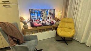 A living room with a television on a wooden stand, a yellow armchair, a grey rocking chair, and a Christmas tree. - GOLD APARTMENT**** in the heart of Pula only 5 minutes from the sea (Pula)
