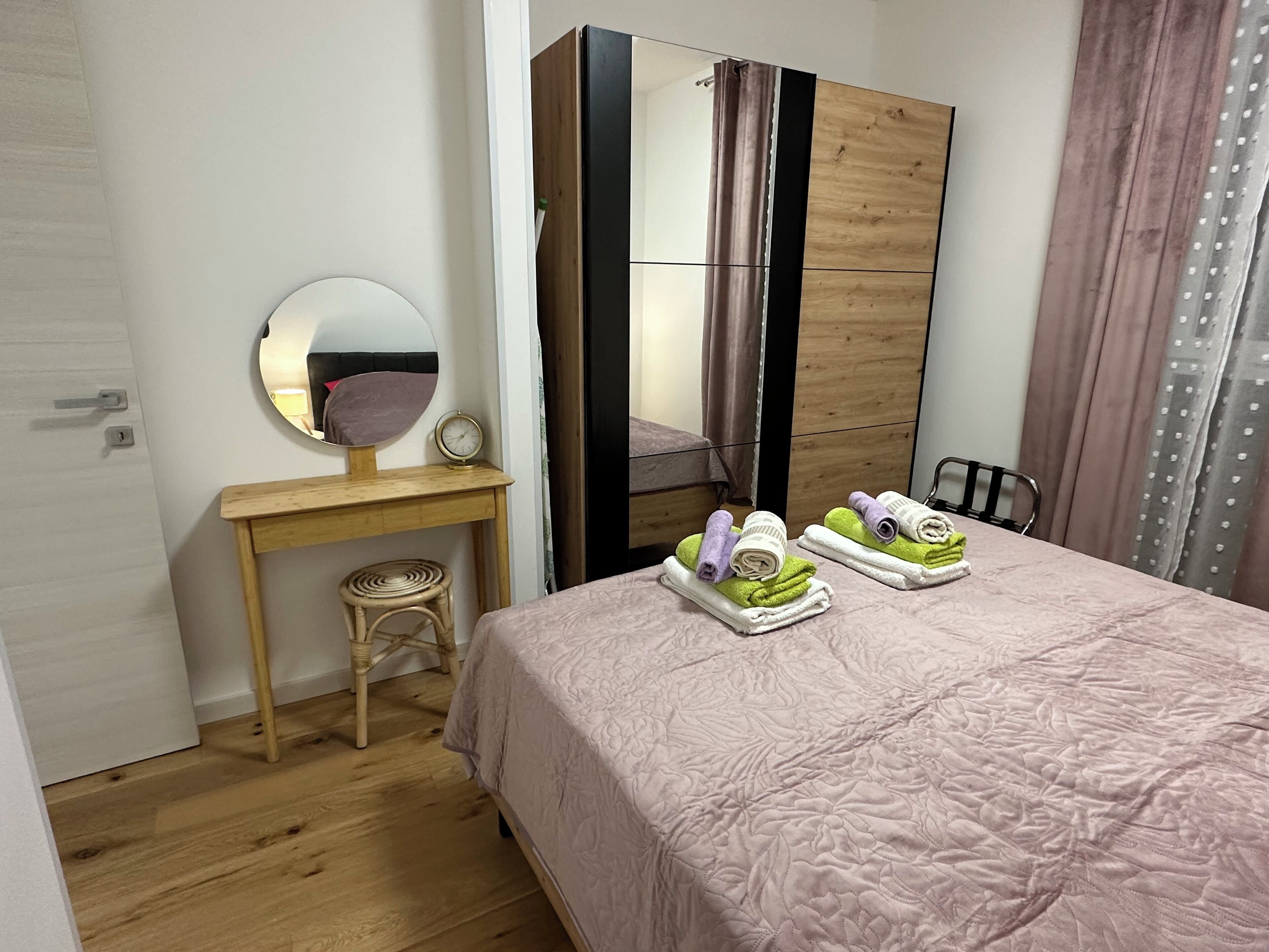 A bedroom with a bed, a wooden desk, a chair, a round mirror, and a wardrobe.