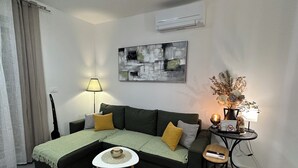 A living room with a sectional sofa, a small round table, a floor lamp, a decorative vase, and an air conditioning unit on the wall. - GOLD APARTMENT**** in the heart of Pula only 5 minutes from the sea (Pula)
