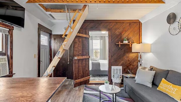 Una habitación con una escalera de madera, un sofá con un cojín que dice 'juntos', una mesita y una lámpara.